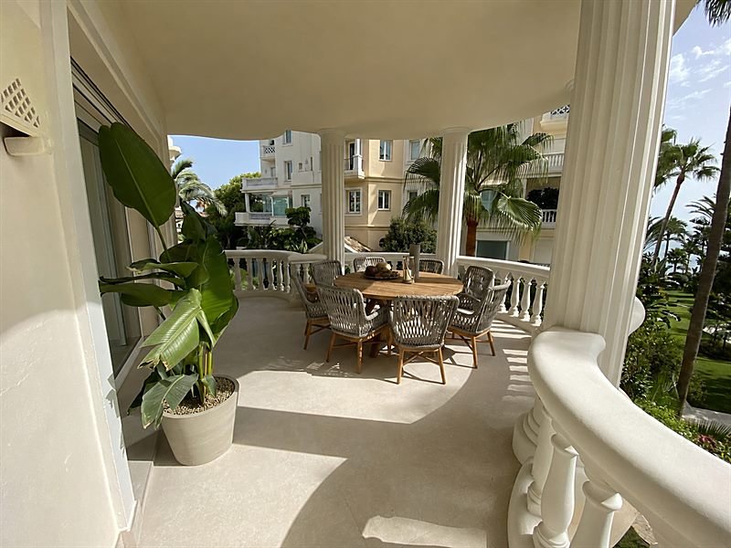 Terraza cubierta con mesa de comedor exterior y palmeras