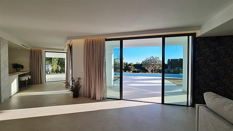 Salón interior con grandes ventanales abiertos a la piscina