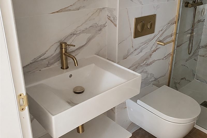 Baño con lavabo sobre encimera, revestimiento de mármol y grifería dorada
