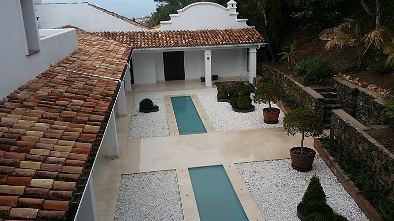 Patio exterior con dos láminas de agua, pavimento de piedra y porche de la casa de invitados