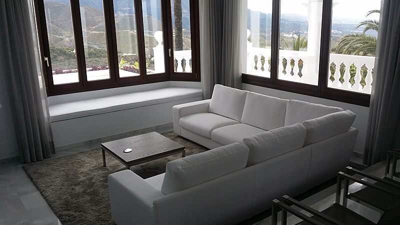 Salón con ventanales de madera y banco corrido bajo la ventana, con vistas a la sierra