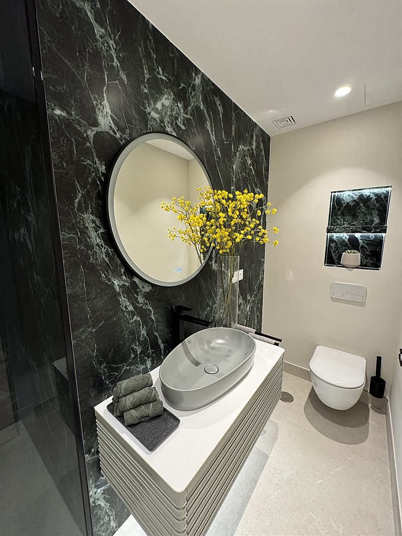 Baño revestido en mármol verde con espejo circular retroiluminado